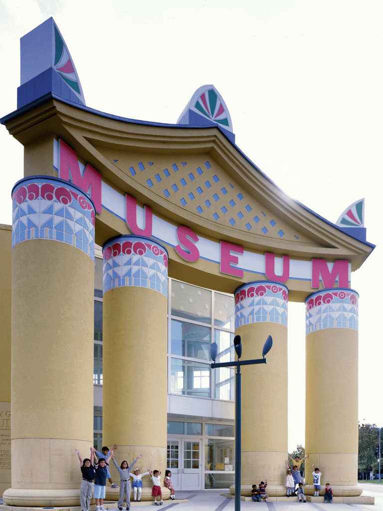 Colorful museum entrance with large columns and children playing outside, showcasing a vibrant cultural experience.