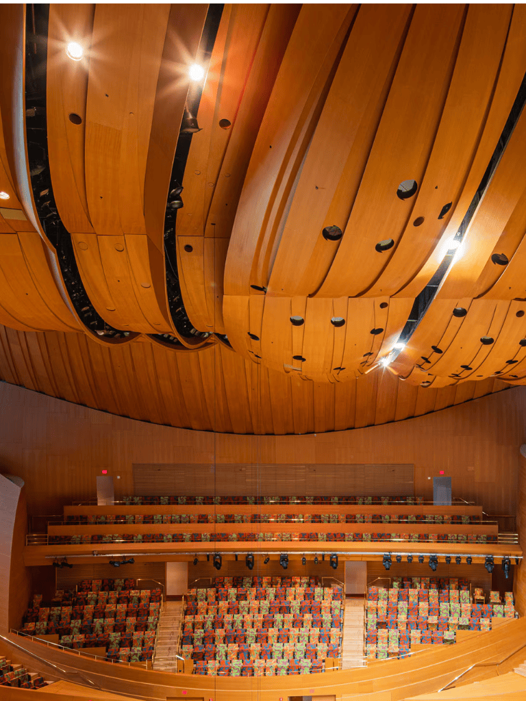 Vibrant theater auditorium with curved wooden ceiling and colorful tiered seating for performances.