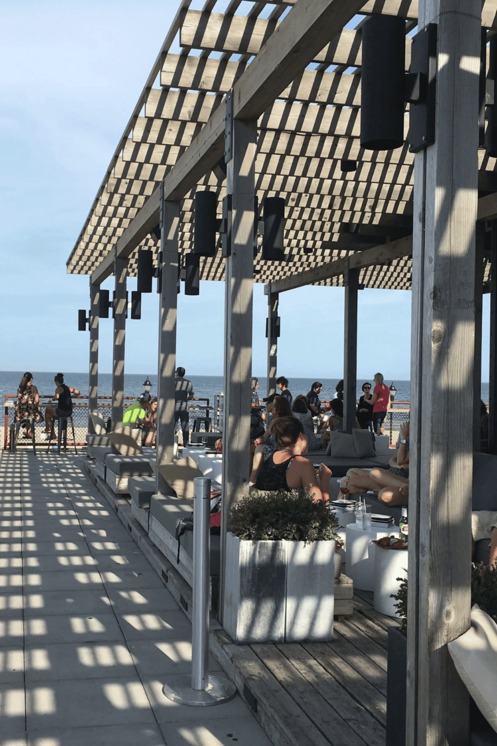 Seaside outdoor restaurant with wooden pergola, ocean view, and social dining atmosphere.