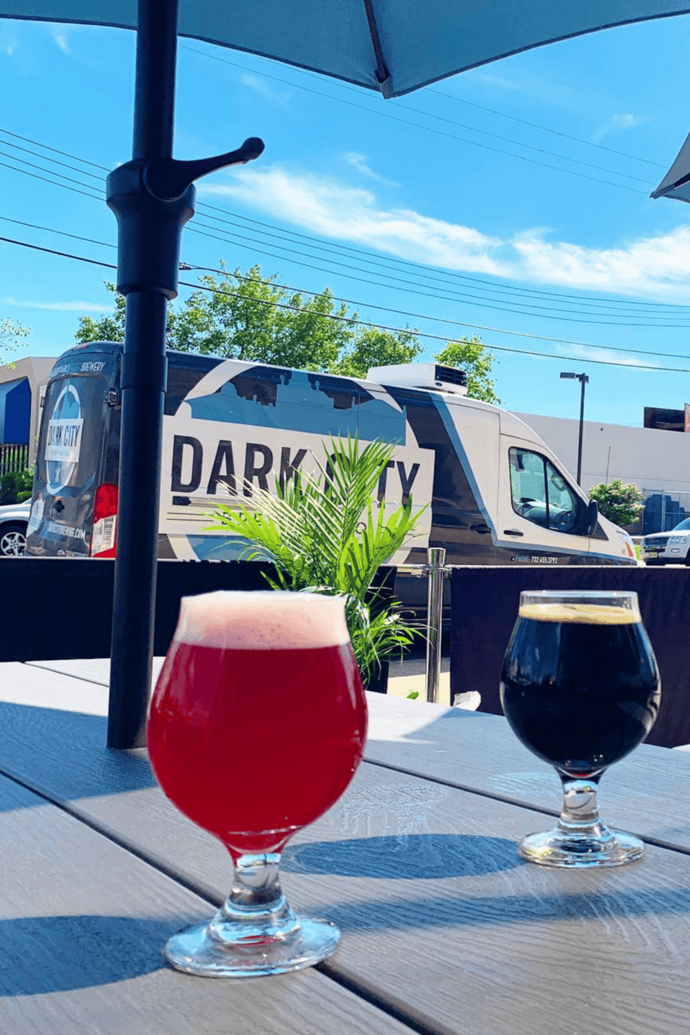 - Bright red and black craft beers served outdoors under umbrellas, with Dark City delivery van in background.