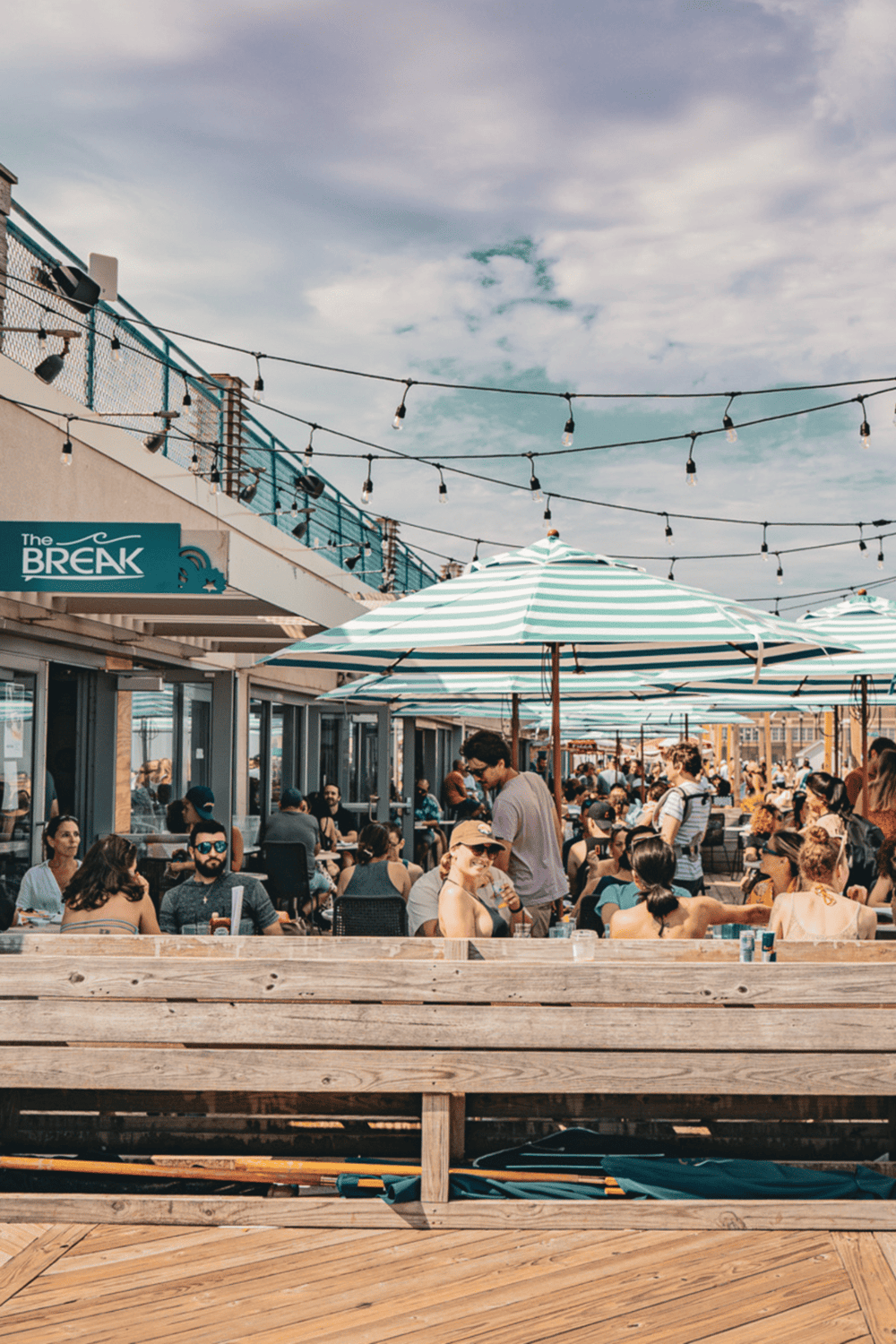 Relaxed outdoor restaurant with string lights and umbrellas, vibrant social scene, perfect for dining and drinks in a lively urban setting.