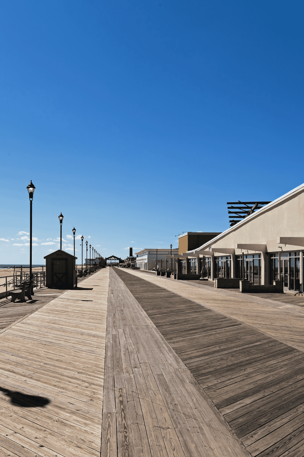 Sunny beach boardwalk with shops and benches, ideal for seaside strolls and coastal relaxation.