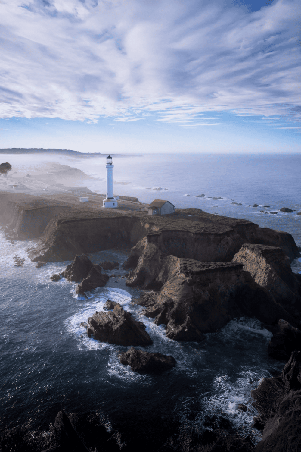 Lighthouse on rugged coast with ocean waves and dramatic sky, scenic coastal navigation aid.