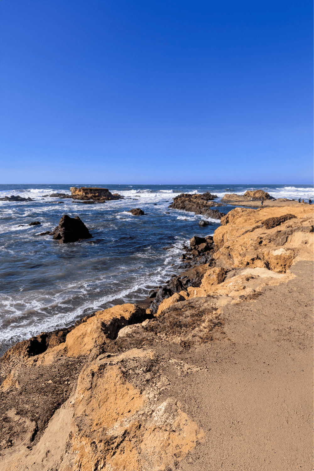 Seaside rocky coast with waves crashing under a clear blue sky, ideal for navigation and travel planning.