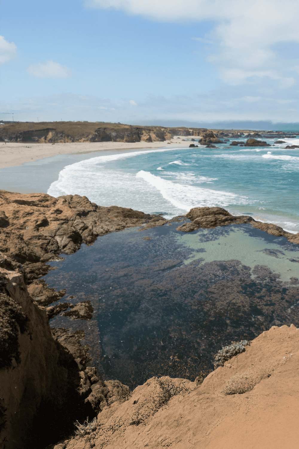 Serene coastal landscape with rocky shoreline, turquoise waves, and sandy beach, ideal for travel and adventure seekers.