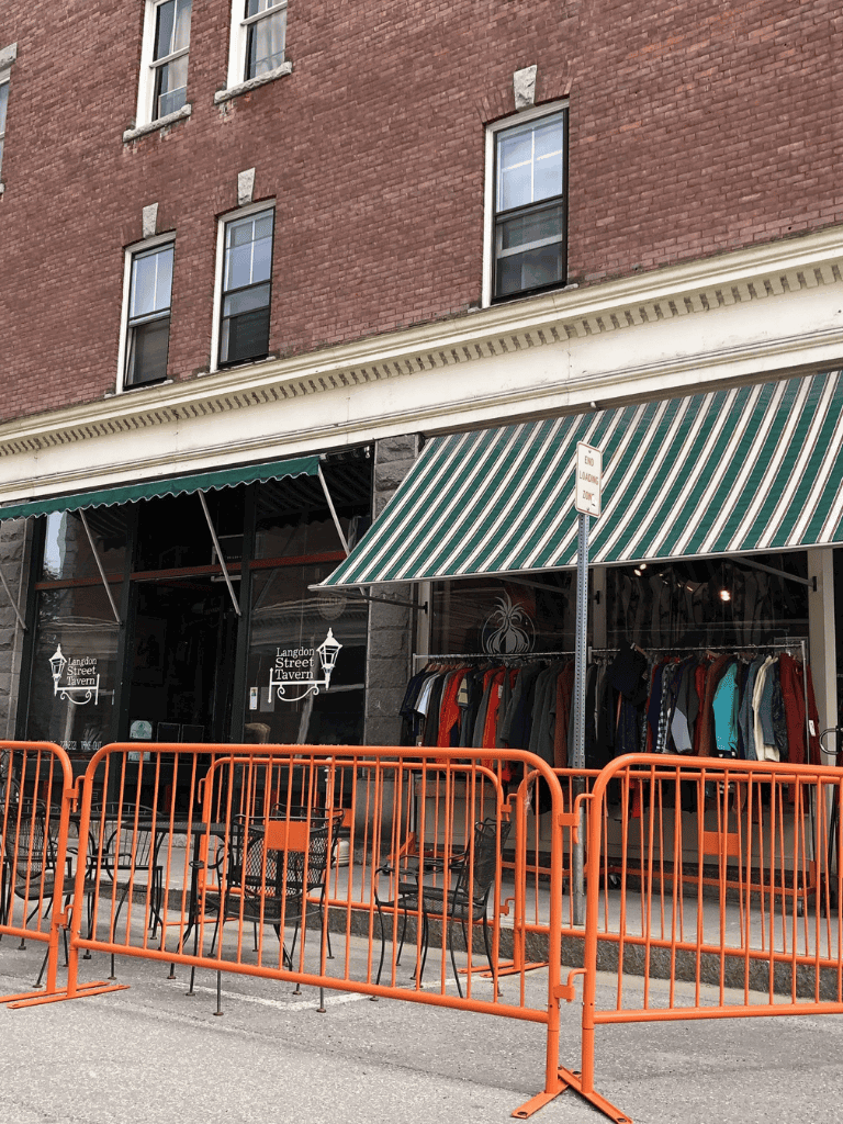 Clothing store outside Langdon Street Tavern with sidewalk seating and orange barricades.