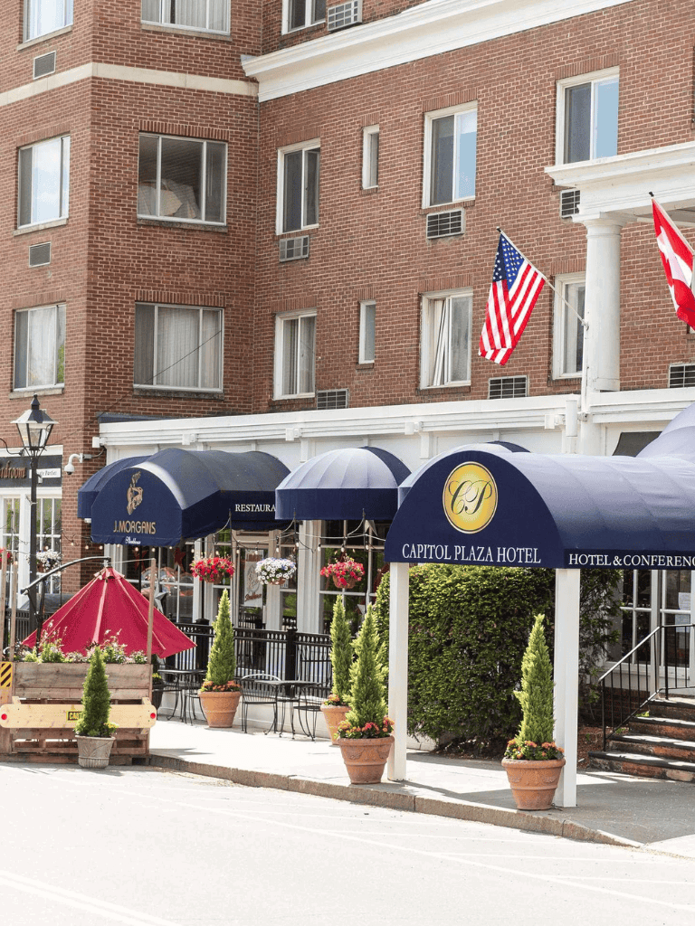 American flag outside Capitol Plaza Hotel, downtown hotel with outdoor seating and potted plants, offering conference and event services.
