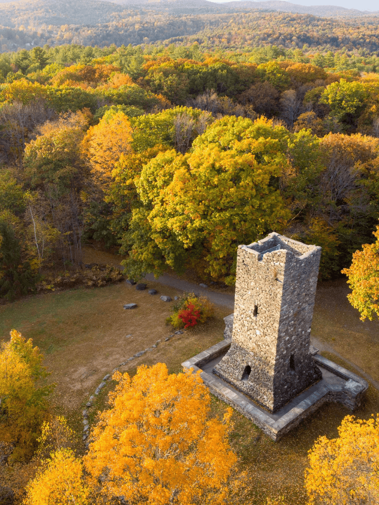 Ancient stone tower surrounded by vibrant autumn foliage and scenic mountain landscape.