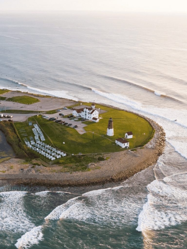 Seaside lighthouse and historic buildings on a coastal island at sunset.