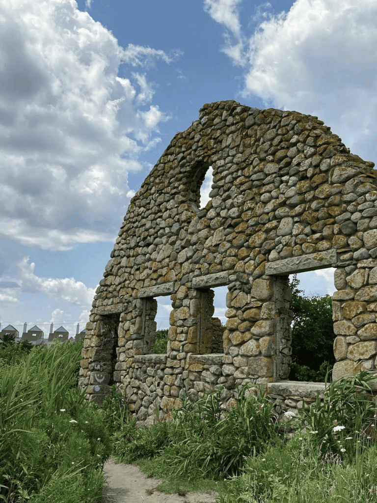 Ancient stone building ruins with an open window and arch, surrounded by greenery and blue sky.
