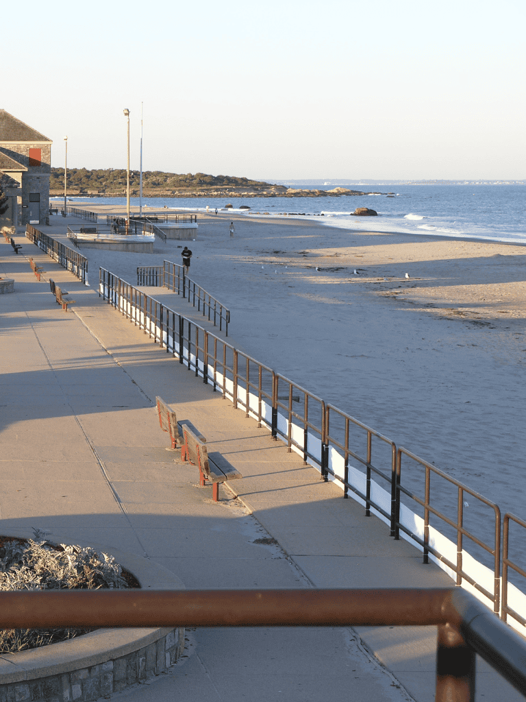 Seaside promenade with benches and railing overlooking the beach and ocean view.