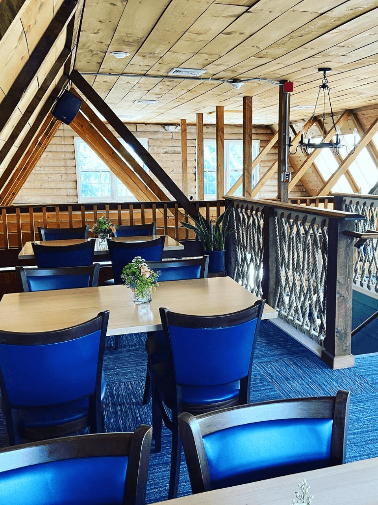 Cozy wooden interior of a restaurant with blue cushioned chairs and natural lighting.