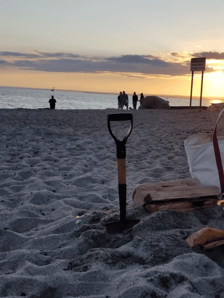 Shovel on sandy beach with sunset, people walking by ocean, QuestForDirections travel destination.