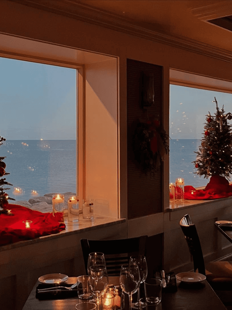 Cozy seaside holiday dining with decorated Christmas trees and candles, overlooking the ocean.