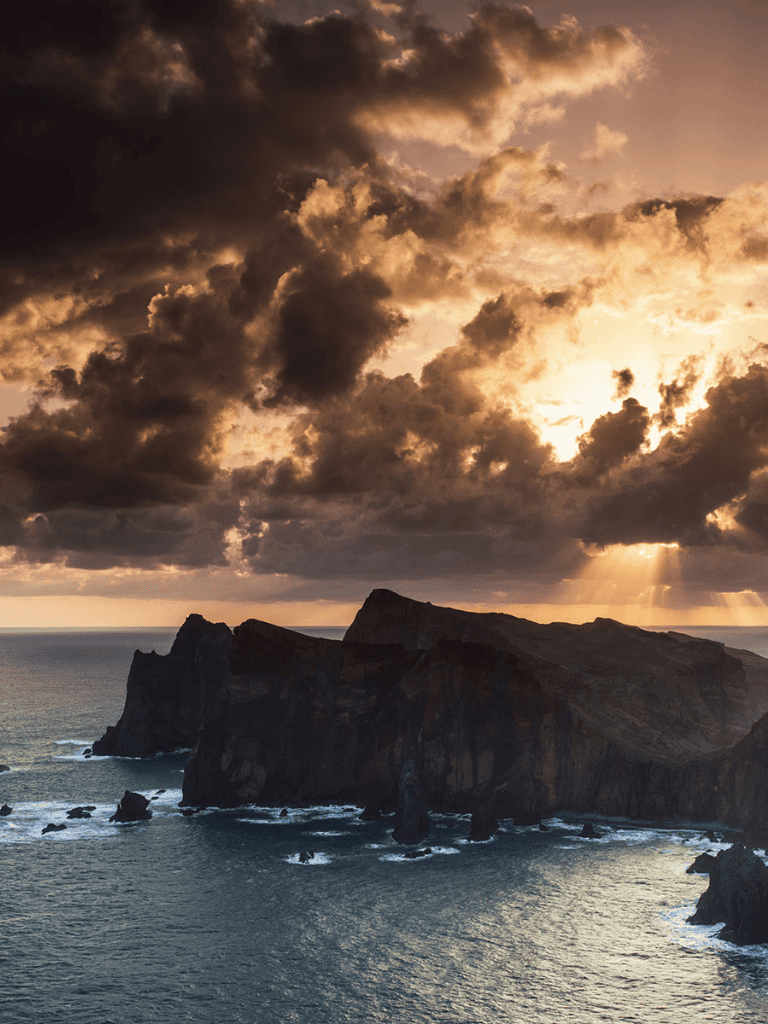 Sunset over rugged cliffs and stormy clouds at a coastal landscape.