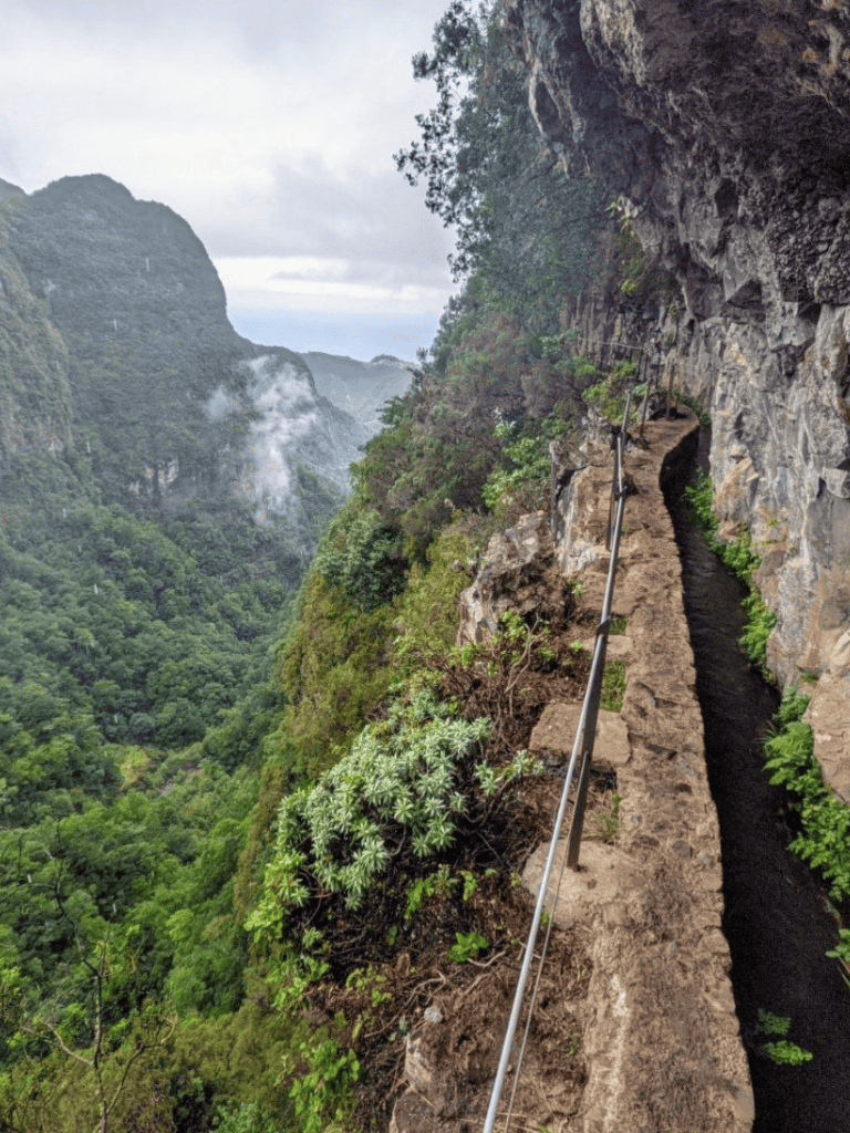 Steep mountainous hiking trail with safety railing overlooking lush green valleys and misty mountains.
