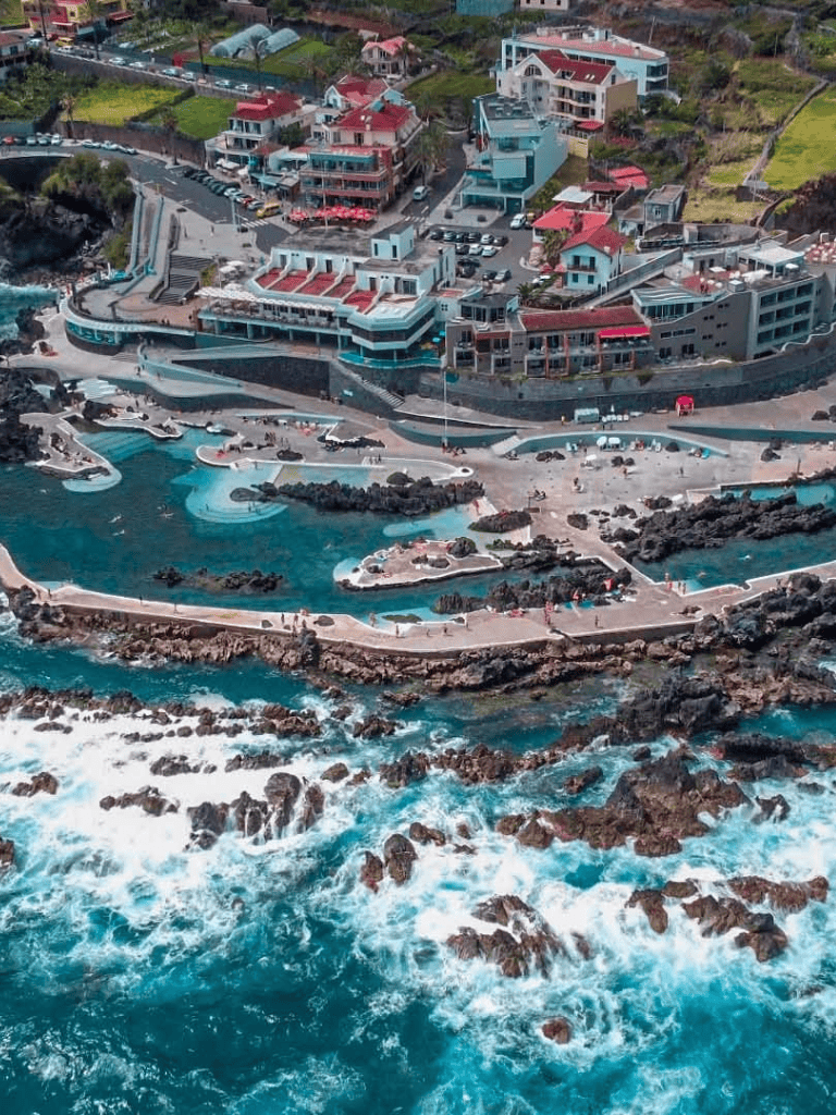 Aerial view of scenic coastal resort with pools, rocky shoreline, and colorful buildings in tropical location.