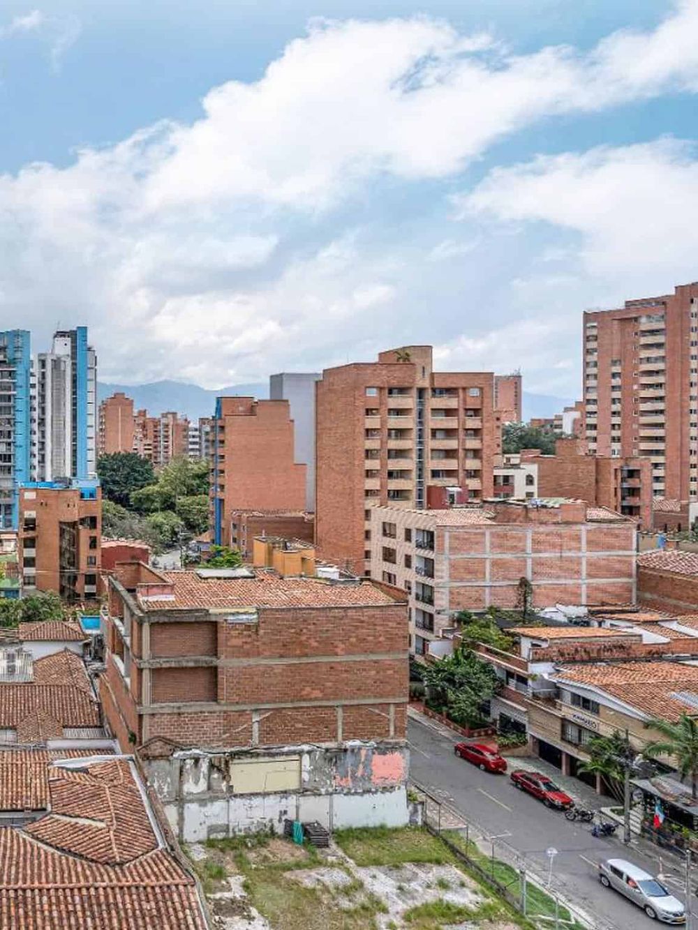 Colorful cityscape with mixed high-rise and low-rise buildings, urban streets, and a partly cloudy sky.