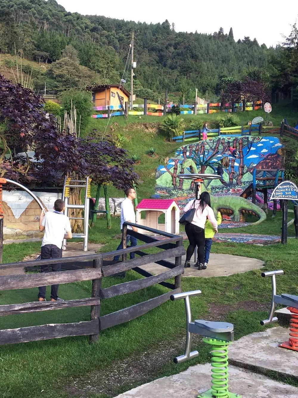 Colorful outdoor playground surrounded by trees and children playing, perfect for family fun and nature exploration.