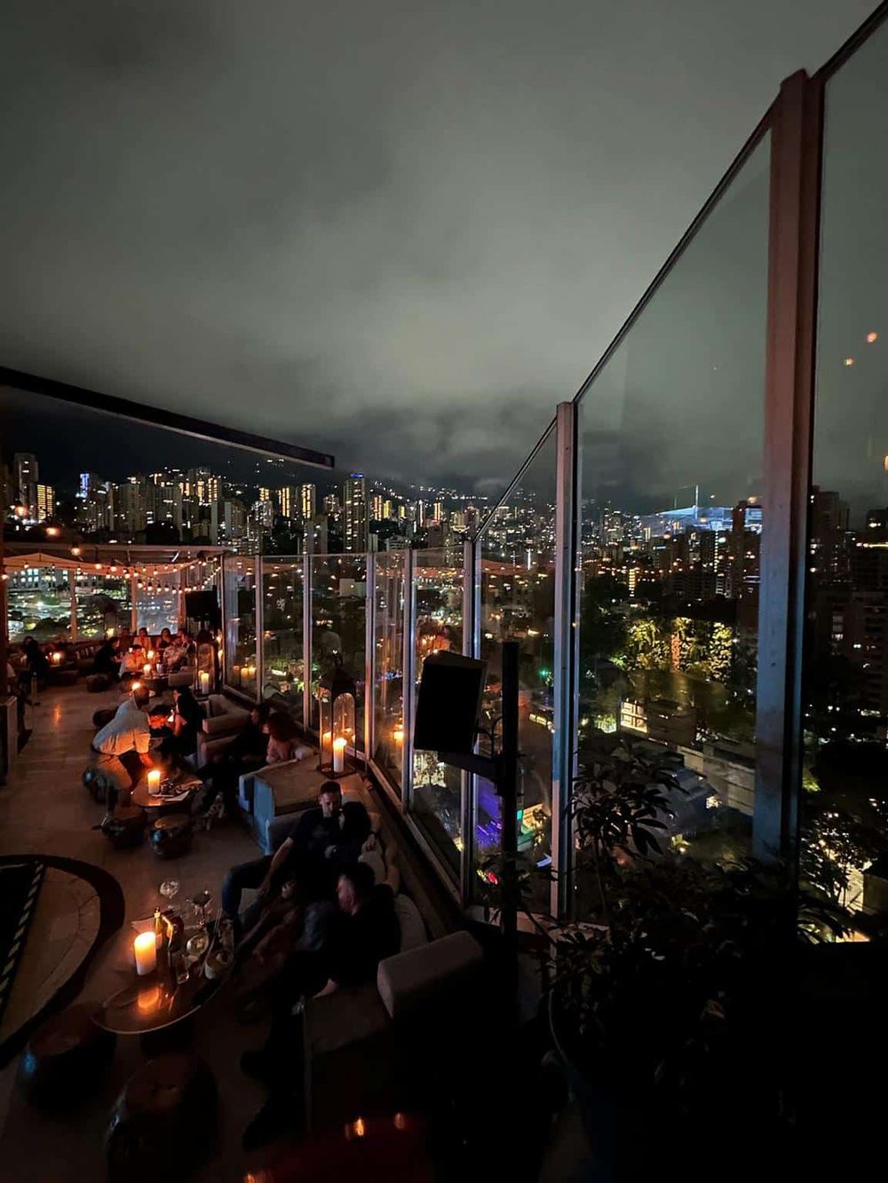 Vibrant cityscape view from a rooftop bar at night, featuring illuminated buildings and a lively social atmosphere.