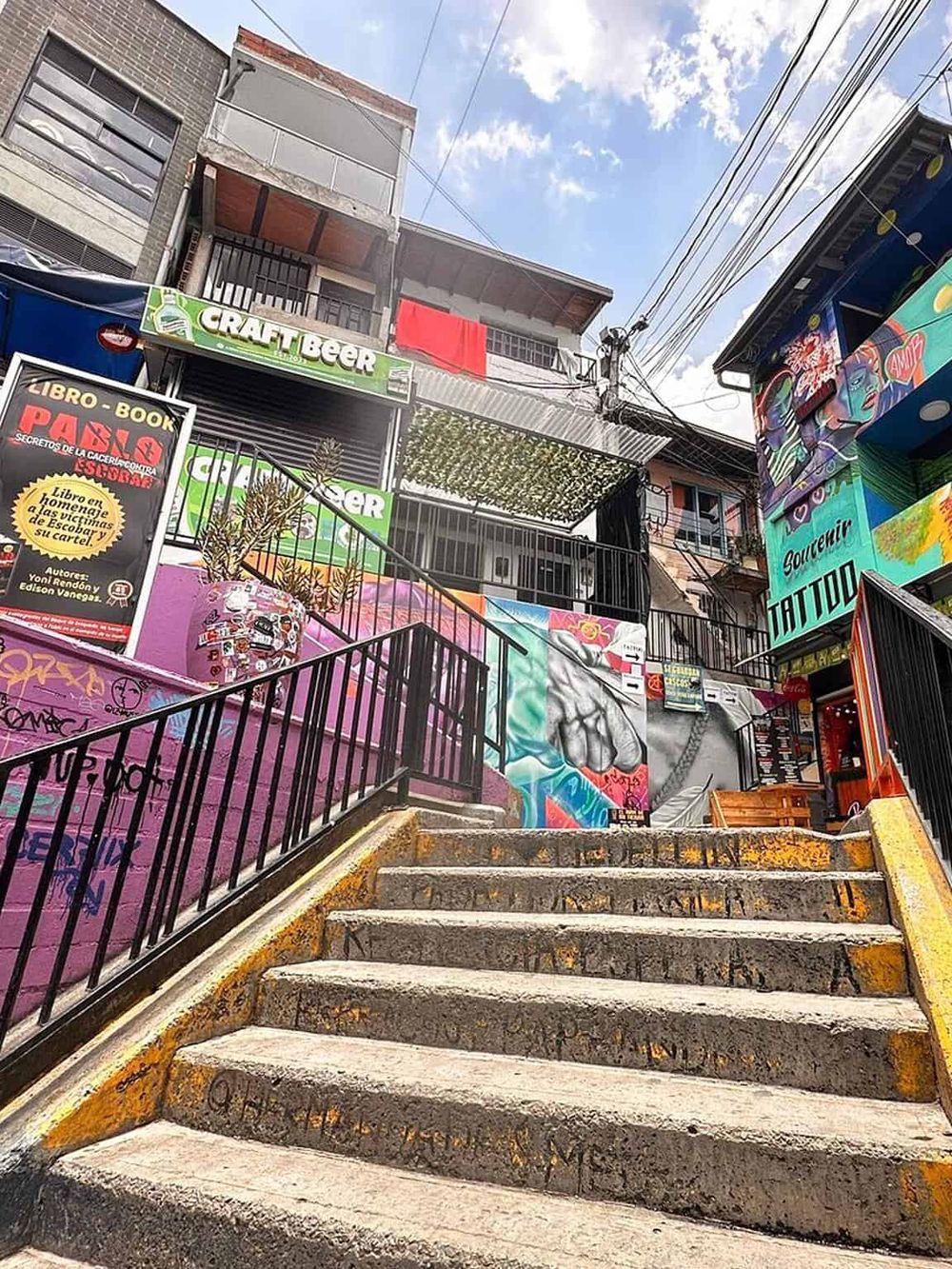 Colorful alley with stairs leading up to a vibrant, graffiti-covered urban setting, showcasing local street art and city life.
