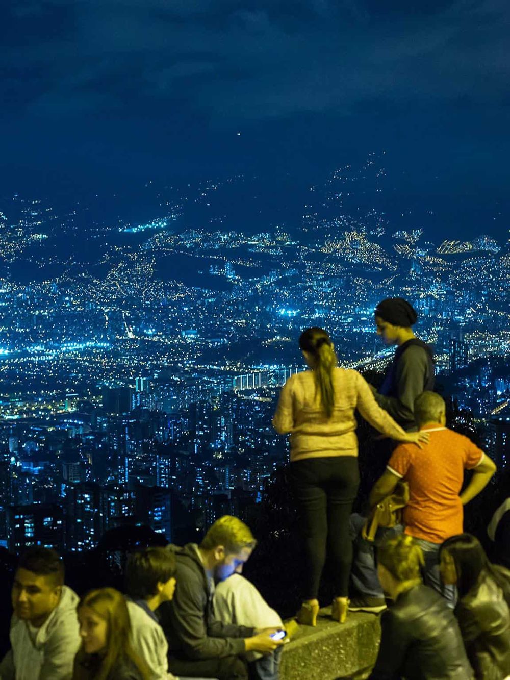 Night city skyline view from a viewpoint with people admiring the city lights and skyline.