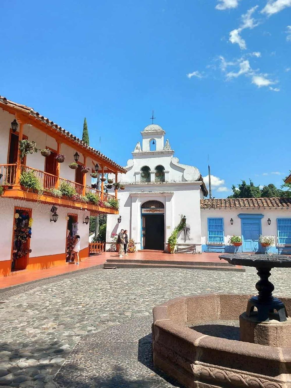Colorful colonial church in a vibrant town square with cobblestone pavement and traditional buildings.