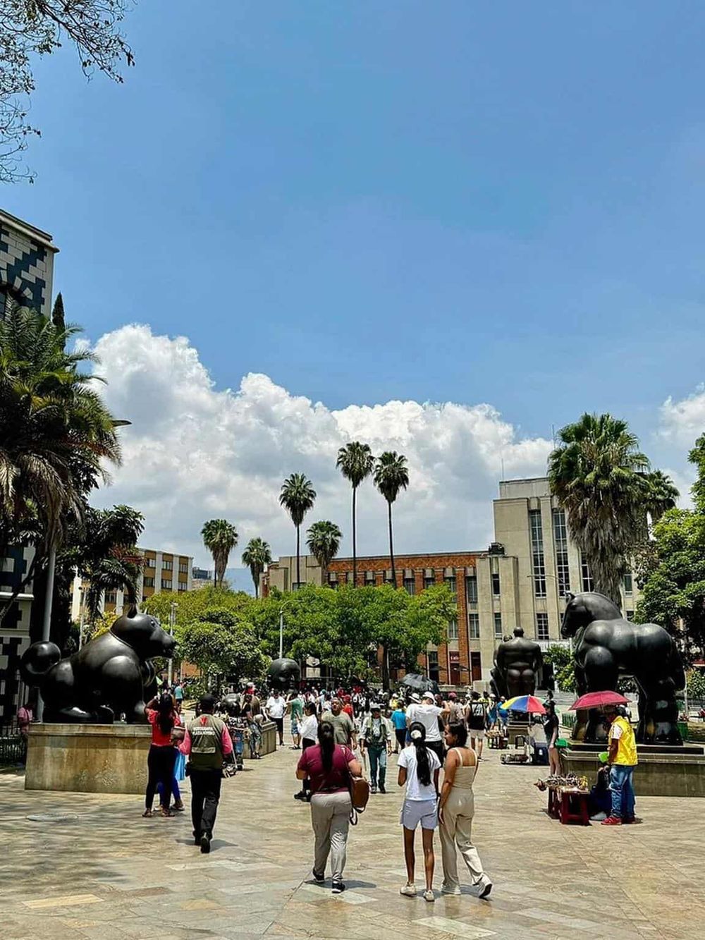 Vibrant city square with sculptures, palm trees, and crowd, perfect for directions and navigation assistance.