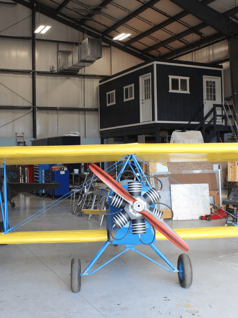 Small aircraft propeller plane in workshop with equipment and model house structure.