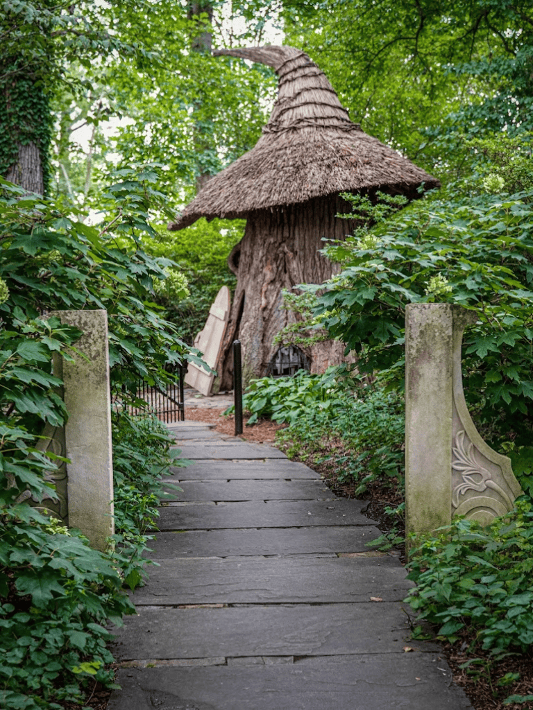 Enchanted woodland path leading to whimsical fairy house with thatched roof and lush greenery.