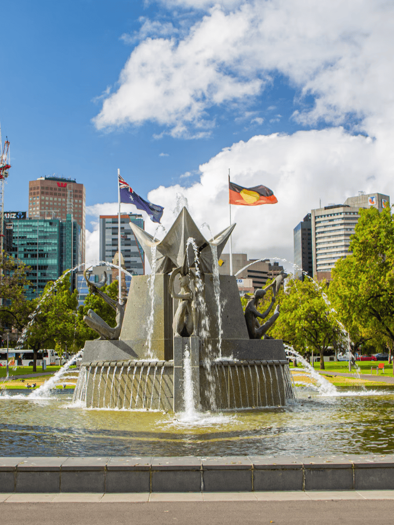 Australia flags at the Quest for Directions fountain in an urban park with city skyline.