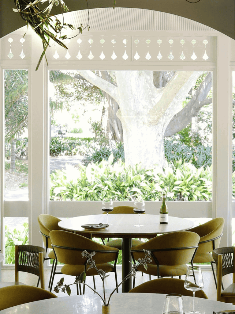 1. Bright dining area with large window view of lush garden and mature tree.