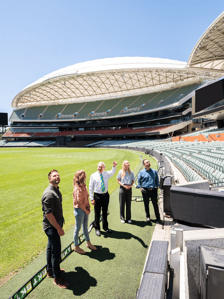 Aerial view of a stadium during tour with group of people on field, modern architecture, green turf, clear sky, Ticketmaster sign, sports venue.