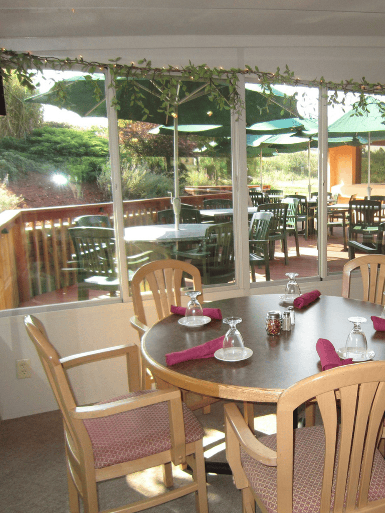 Cozy restaurant dining area with outdoor patio, wooden tables, and green umbrellas, perfect for dining and relaxing.