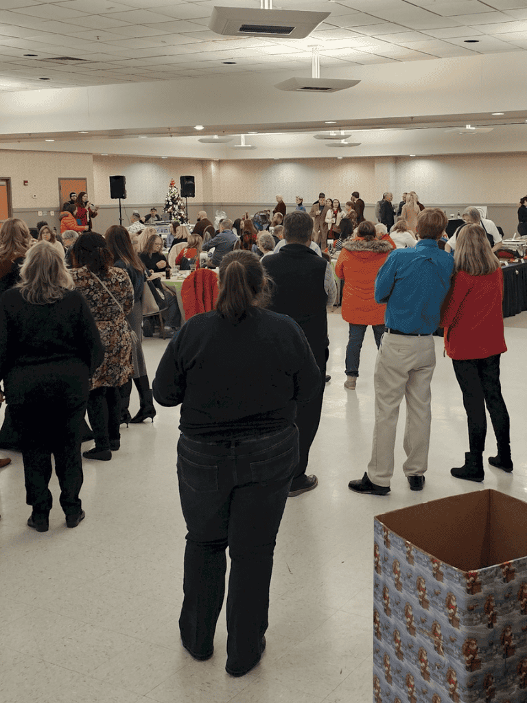1. People gathered at indoor community event with Christmas decor and speaker system.