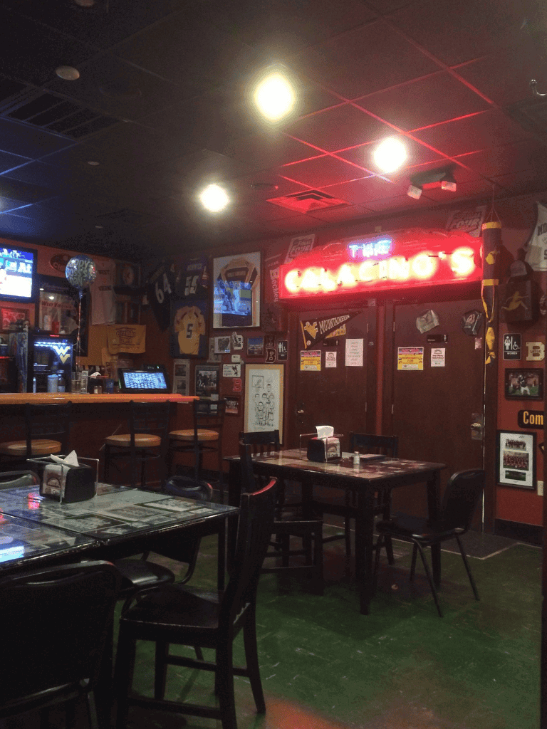 Cozy sports bar interior with neon sign, TV screens, and framed jerseys, perfect for sports enthusiasts and casual dining.