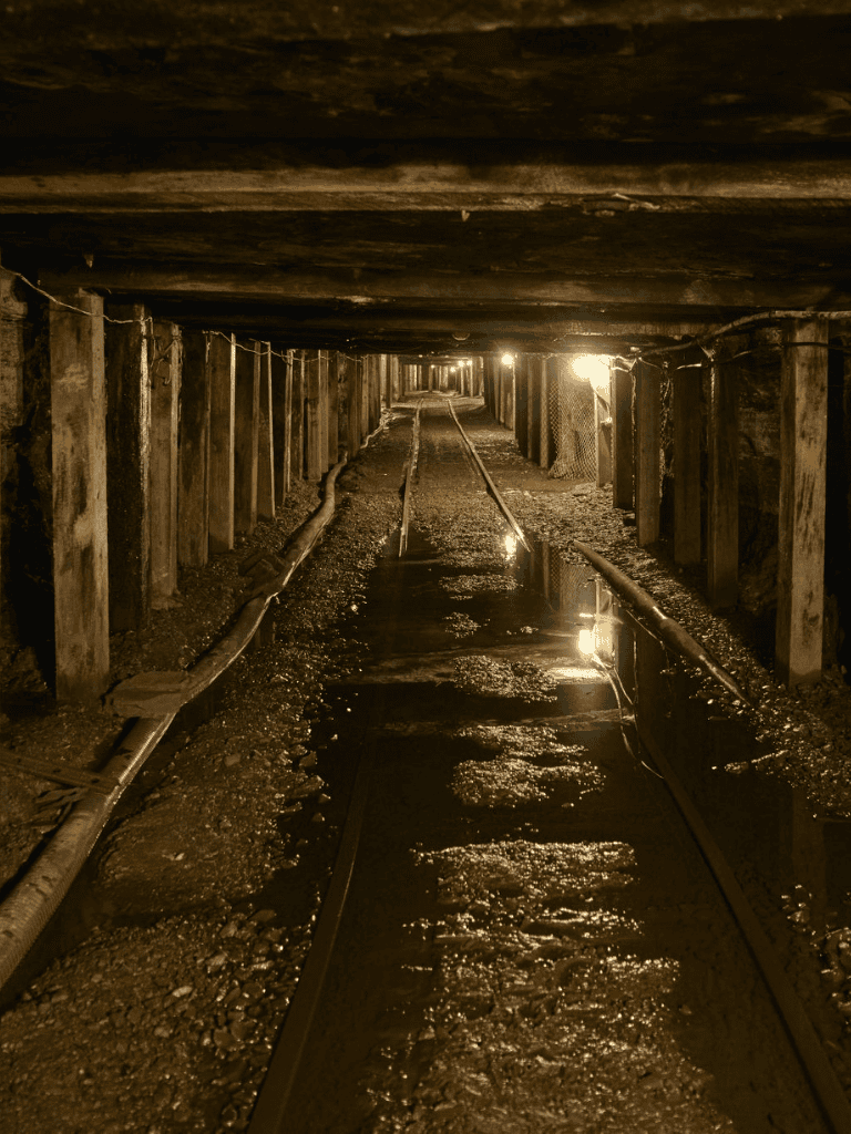 Underground mine tunnel with rails and dim lighting for exploration and safety.