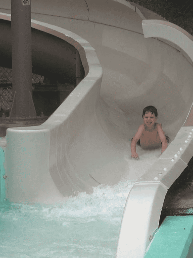 Excited boy enjoying a thrilling ride down a water slide at QuestForDirections Waterpark.