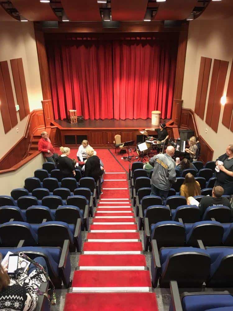 Comfortable theater with stage, red velvet curtains, and engaging musical rehearsal setting.