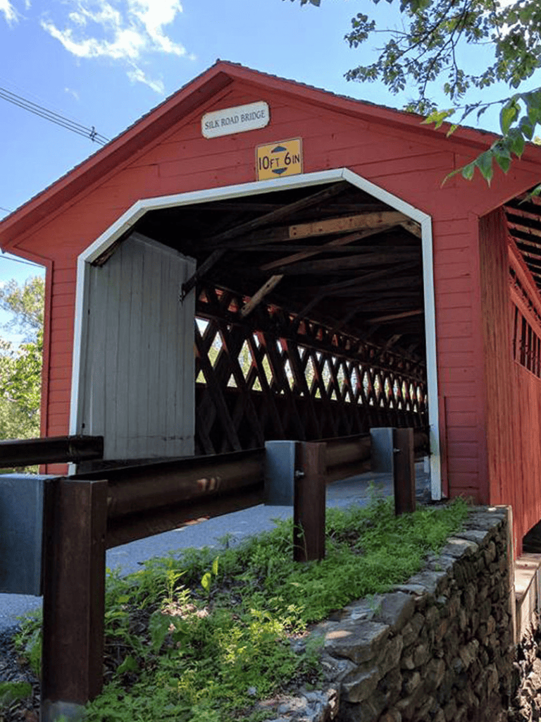 Old Red Covered Bridge with signage and lush greenery, historic wooden structure in scenic area.