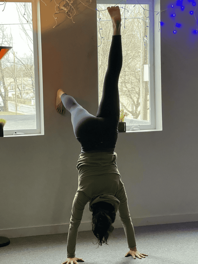 Handstand yoga pose indoors with windows, natural light, and decorative lights.