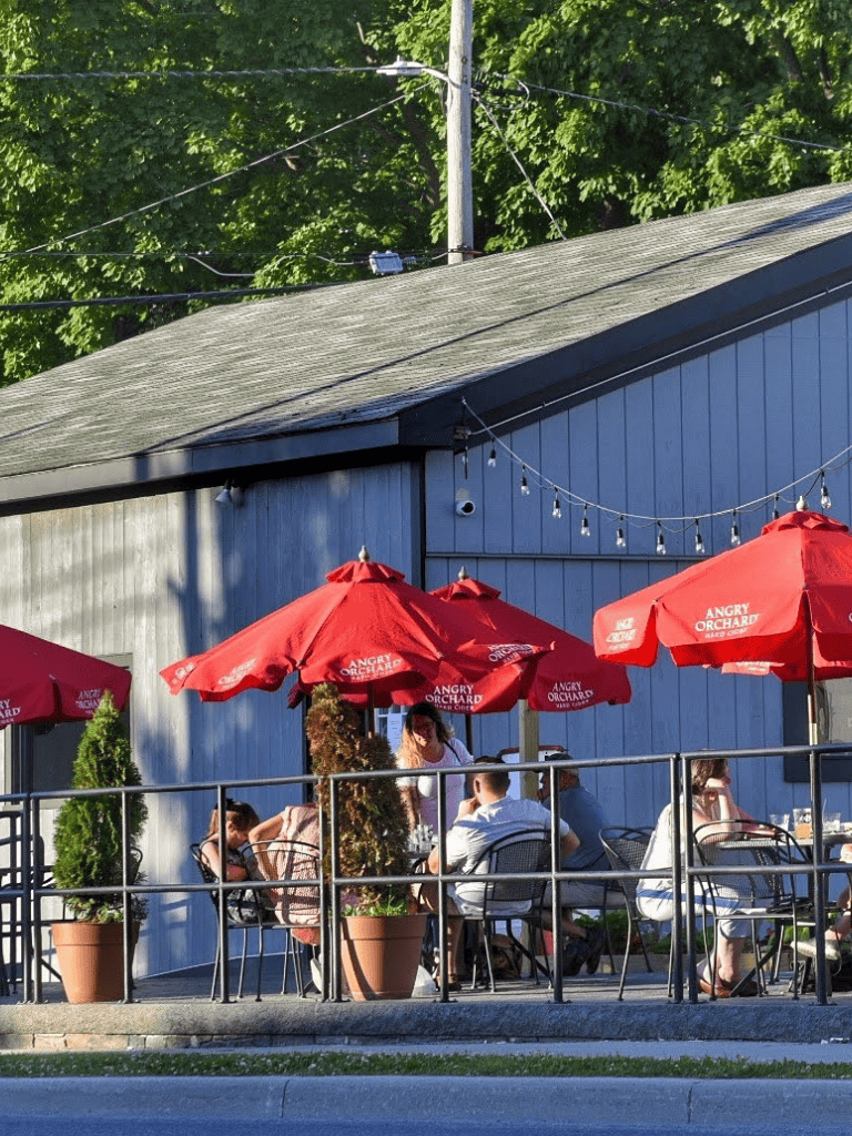 Outdoor dining at Quest for Directions restaurant with red umbrellas and customers enjoying a sunny day.