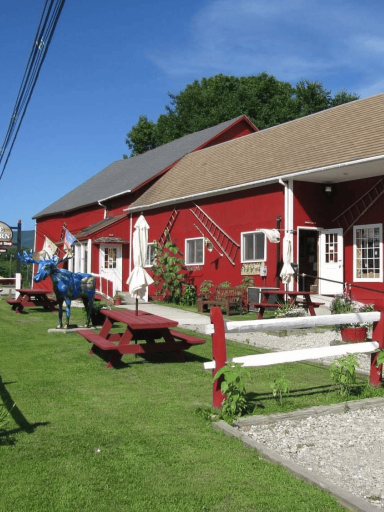 Colorful red barn with outdoor seating and decorative horse statue, perfect for countryside dining.