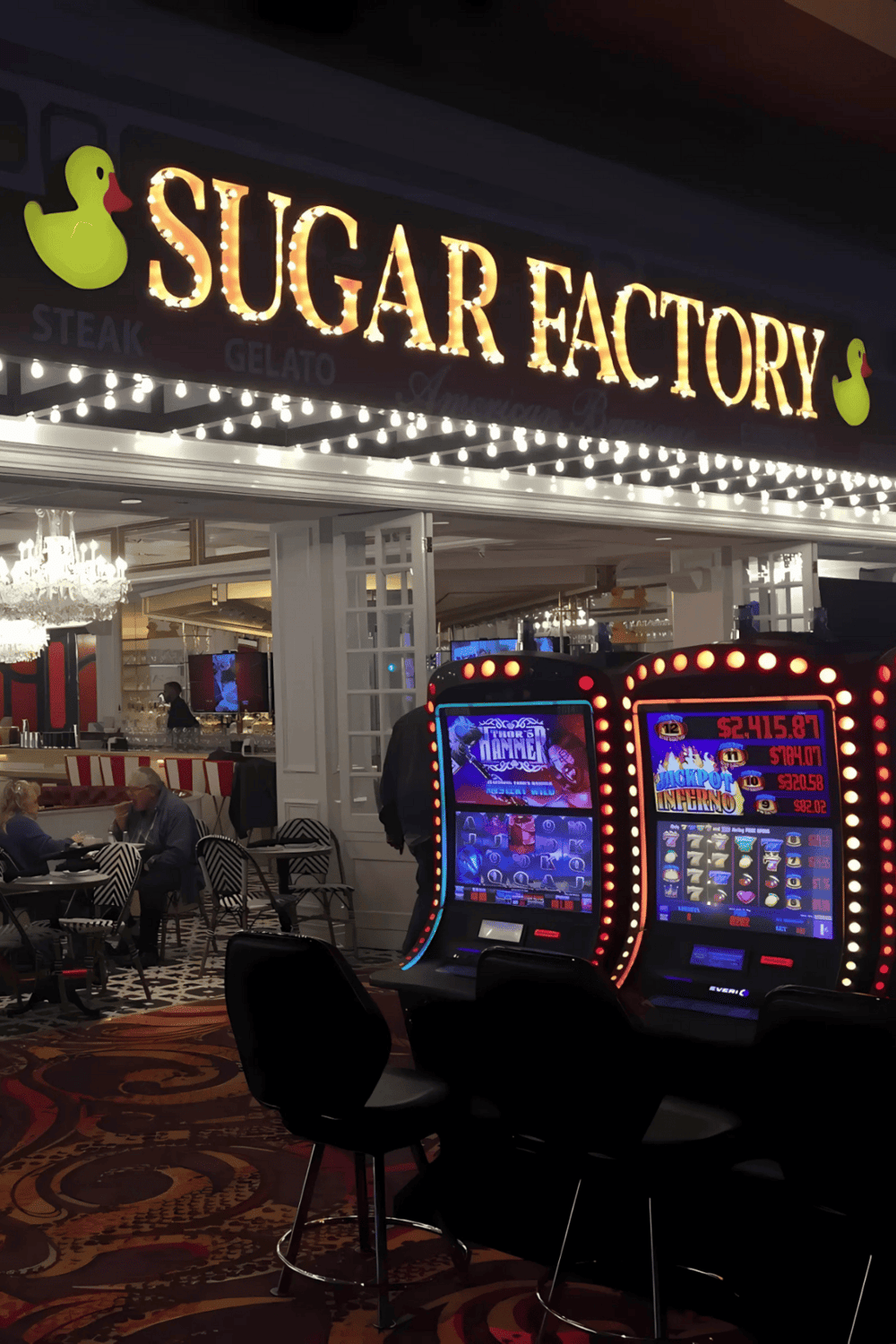 Brightly lit Sugar Factory sign with neon lights and a playful duck logo, inside a lively casino and dining area.