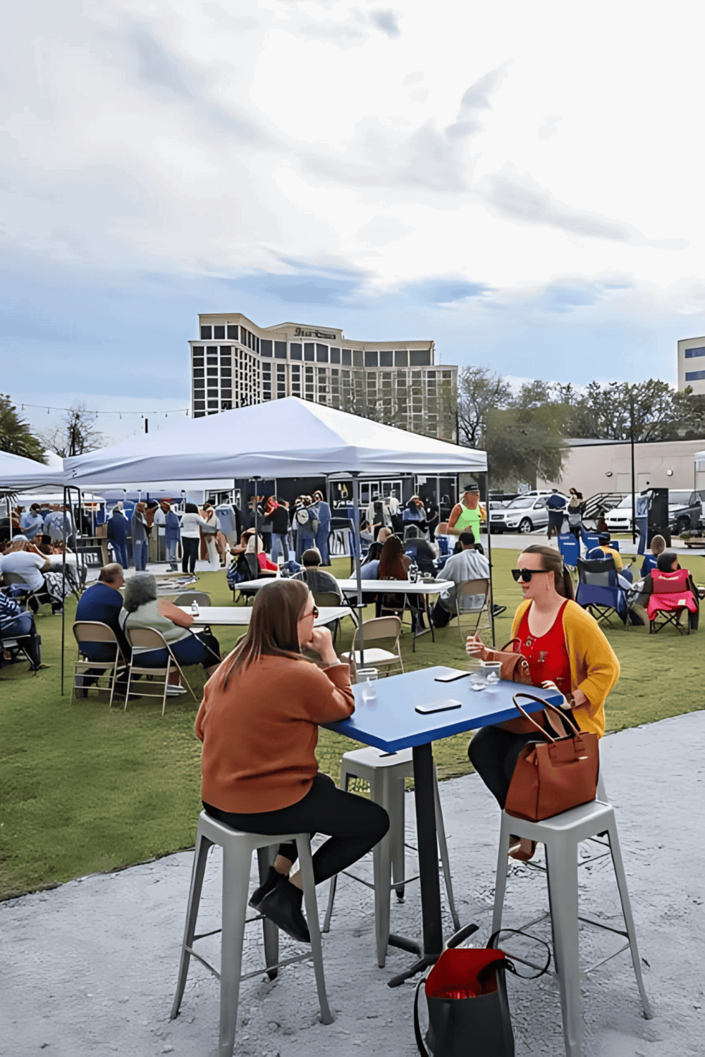 Outdoor event with people, tents, and city skyline in background.