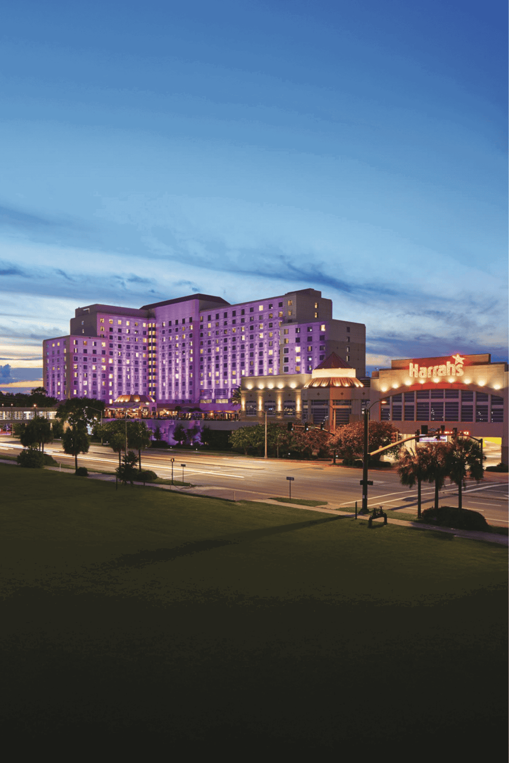 Lavender-colored hotel at night with Harrah's sign, illuminated skyline, vibrant cityscape, QuestForDirections.