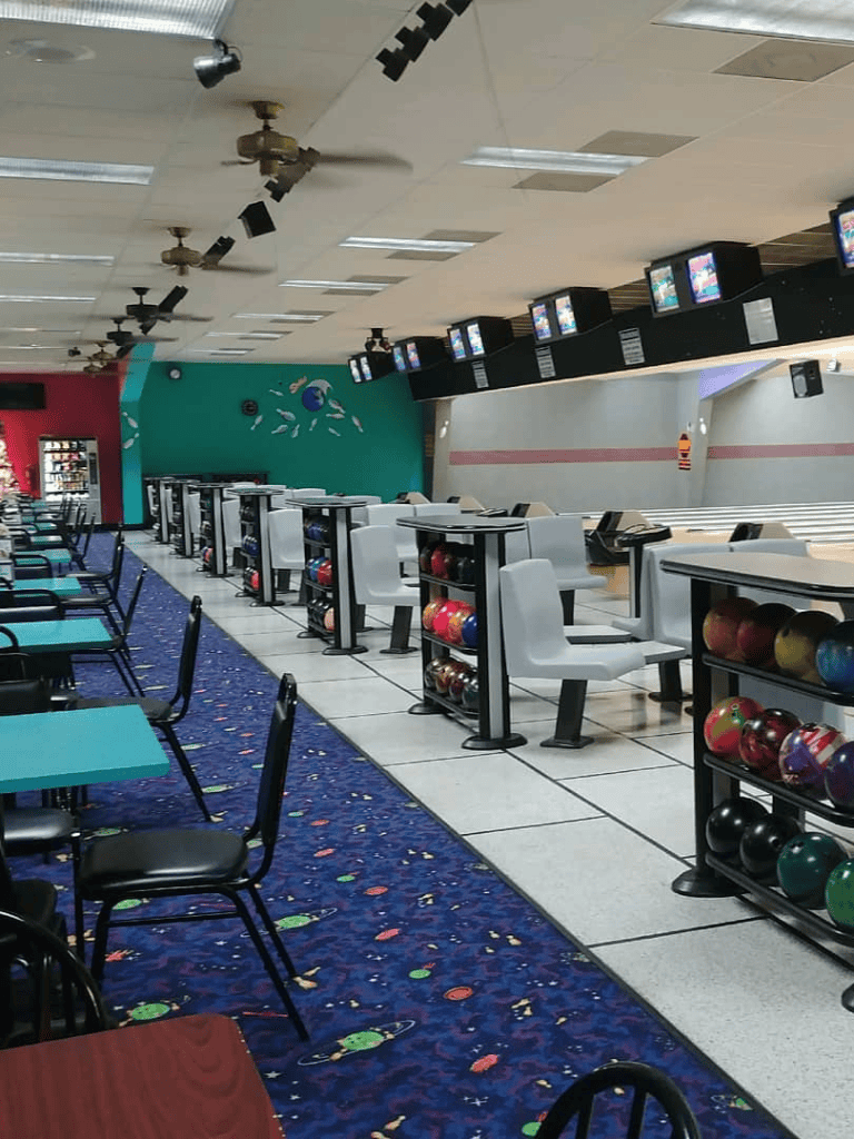Colorful bowling alley with seating area, bowling lanes, and overhead monitors for scoring and gameplay.