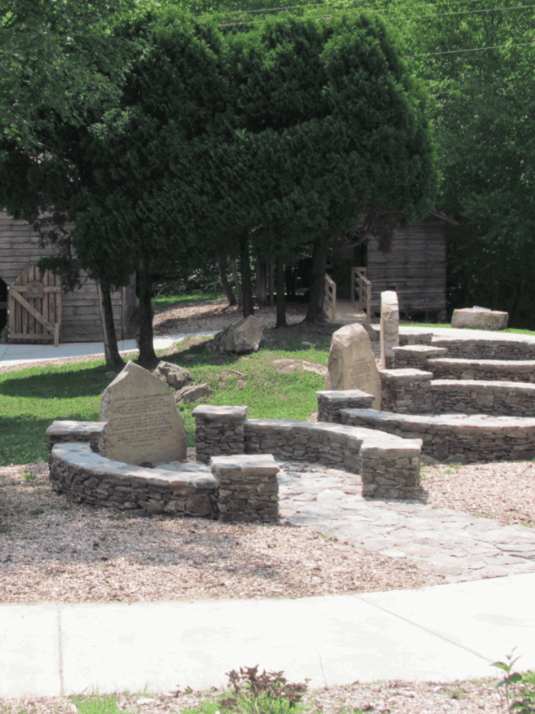 Stone memorials and seating with historic significance, surrounded by lush trees and a peaceful outdoor setting.