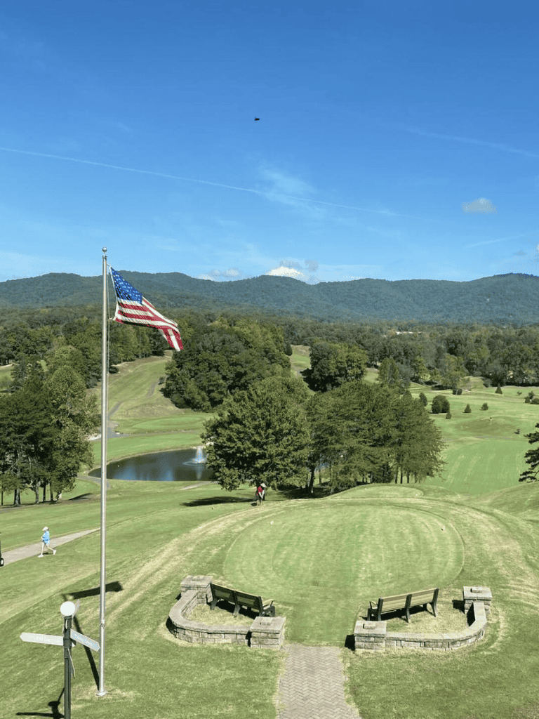 American flag on a golf course with scenic mountain views and walking paths during daytime.
