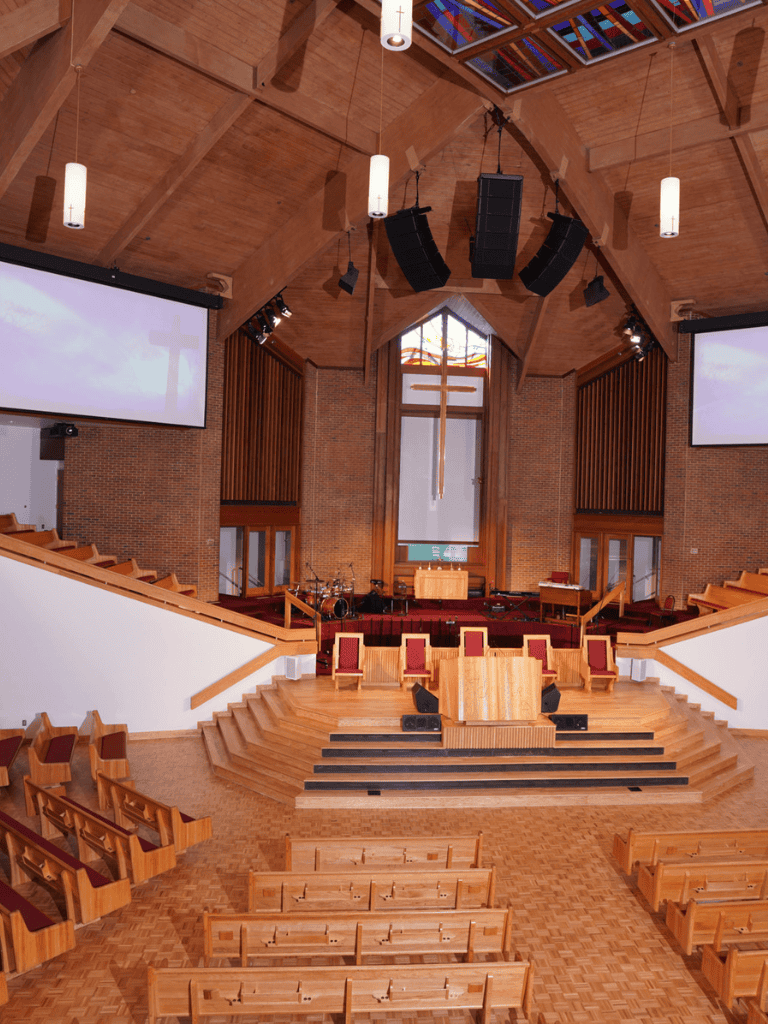 Altar and stage inside church with wooden pews and large cross in the background.